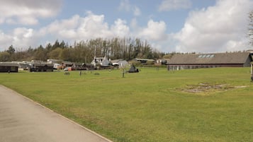 Un campo cubierto de césped con un edificio, mesas de picnic y un cielo despejado.