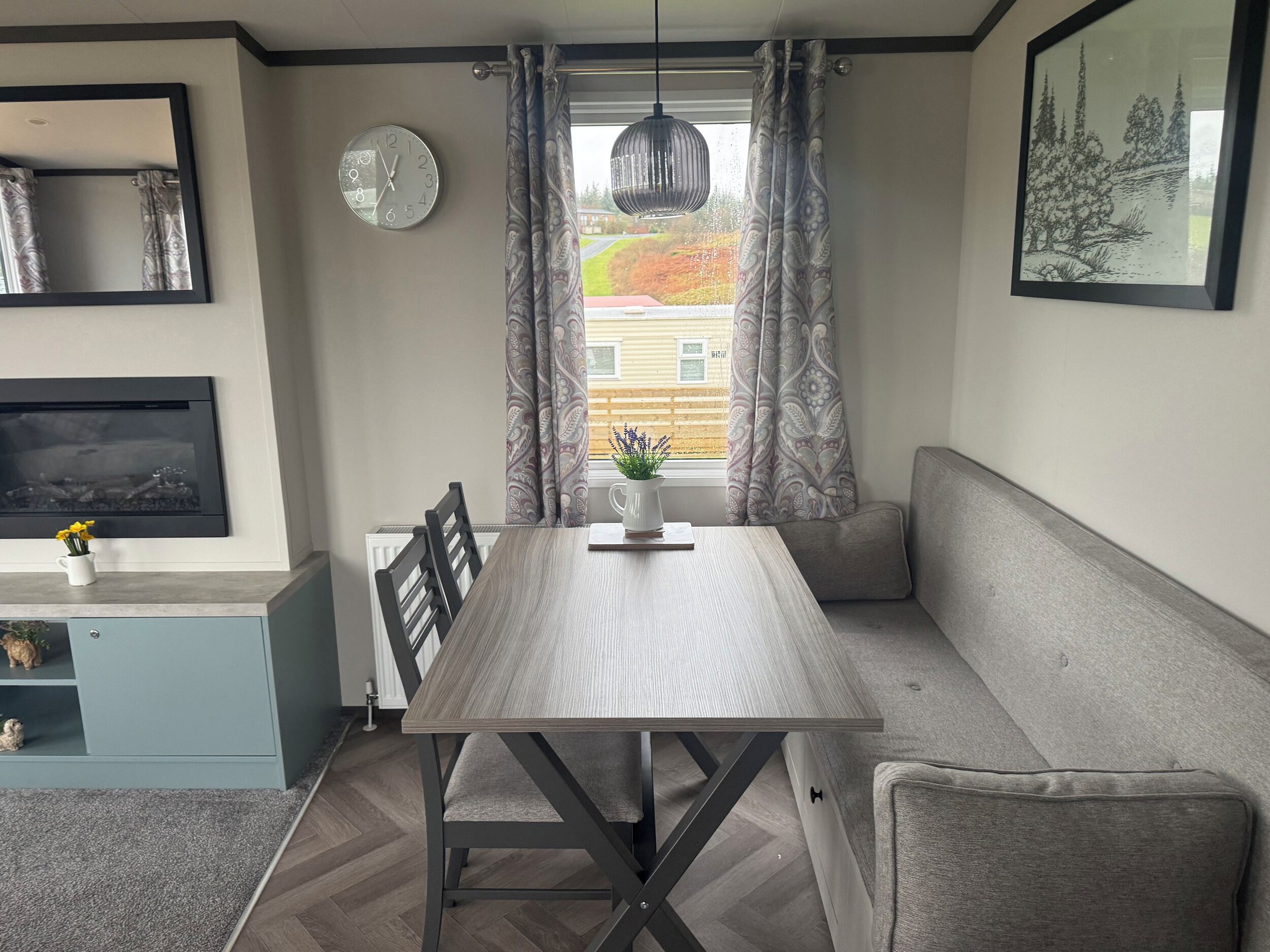 A modern interior with a dining table, a sofa, a TV, a clock, and a window with curtains.