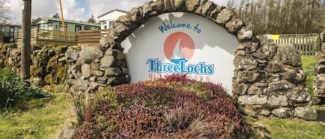 A stone archway with a welcome sign for Three Lochs Hotel Park.
