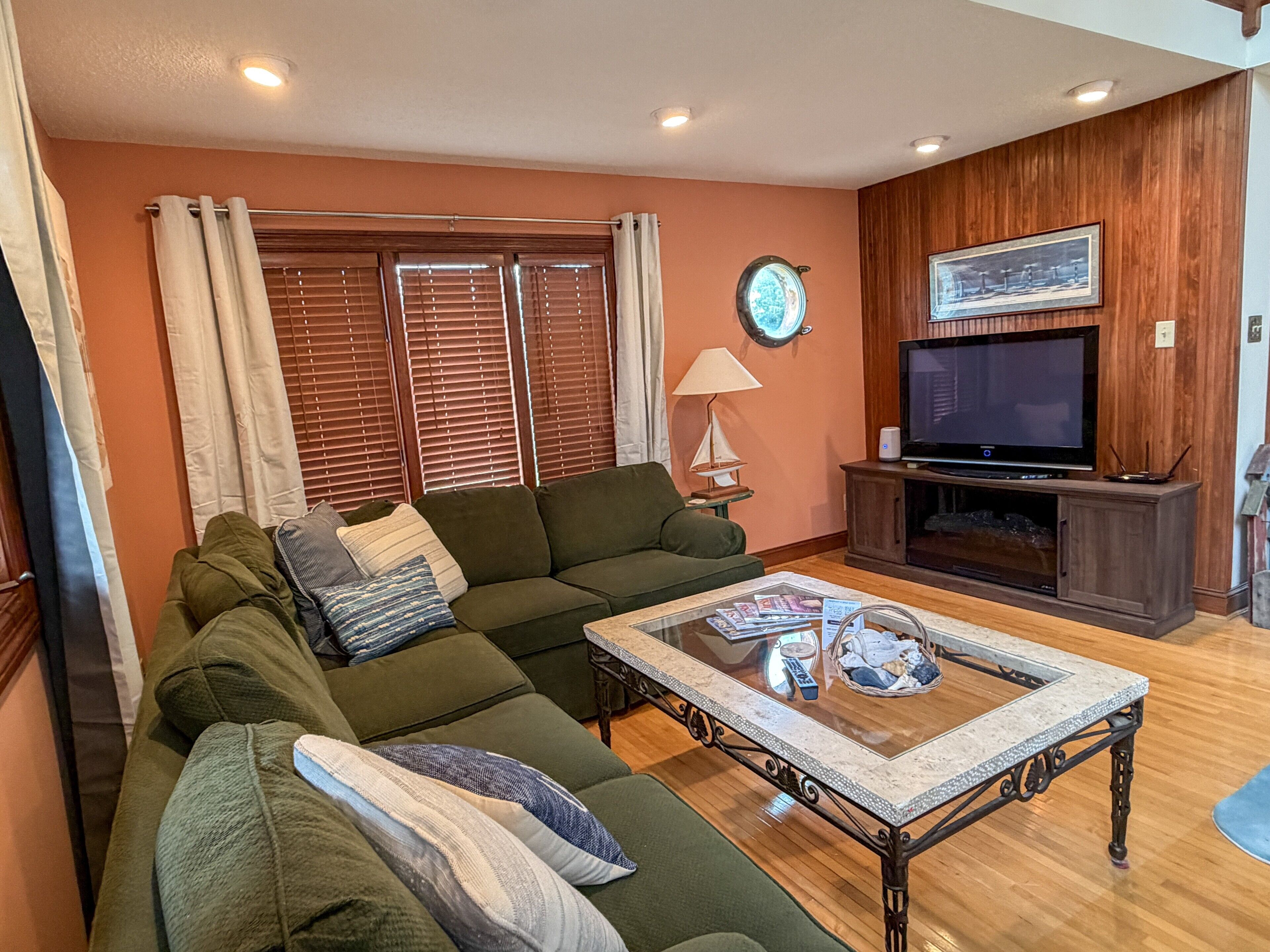 A living room with a green sofa, a coffee table, a television, and wooden paneled walls.