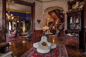 A grand room with a large armchair, a staircase, and a wooden cabinet with decorative items.