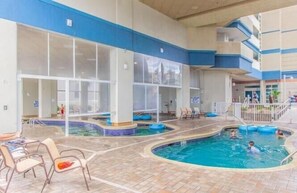 Un espace piscine intérieure comprenant plusieurs bassins, des chaises longues et un espace de repos abrité.