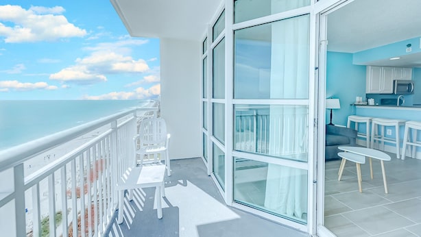Ein Balkon mit Blick auf den Ozean, ein Essbereich mit Tisch und Stühlen sowie eine Küchenzeile mit Mikrowelle und Schränken.