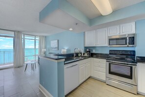 A kitchen with white cabinets, a black countertop, a microwave, an oven, and a dishwasher. - Direct oceanfront 1BR suite with sweeping 14th‑floor views, private balcony, full kitchen & in‑unit washer/dryer. Enjoy resort amenities (pools, hot tubs, lazy river, rooftop pool) & easy beach access—all in a walkable location near top attractions. (Myrtle Beach)