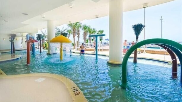 Un espace piscine intérieure doté de toboggans, de palmiers et d’un espace salon abrité.