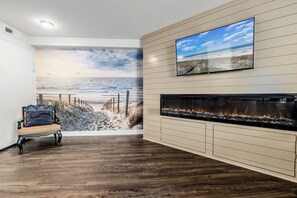 Ein Zimmer mit Meeresblick-Wandgemälde, einem Flachbildfernseher, einem Kamin und Holzboden.