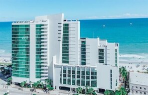 Ein modernes Hotel mit mehreren Etagen, großen Fenstern und Blick auf den Strand.