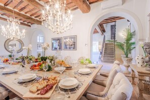 A dining area with a long table set for a meal, chandeliers, and a staircase in the background. - 10 Bedroom Luxury Villa in Lucca (Lucca)