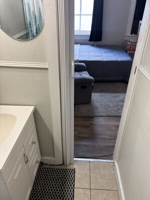 Casa de banho com lavatório, espelho e vista para um quarto com cama e janela.