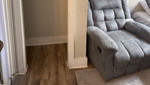 Una habitació amb una poltrona gris, un armari ple de roba penjada i un sòl de fusta.