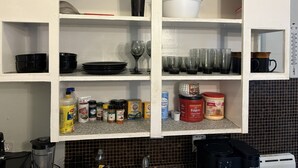 Cuina amb prestatges que contenen diversos utensilis de cuina, una cafetera i una varietat d'aliments.