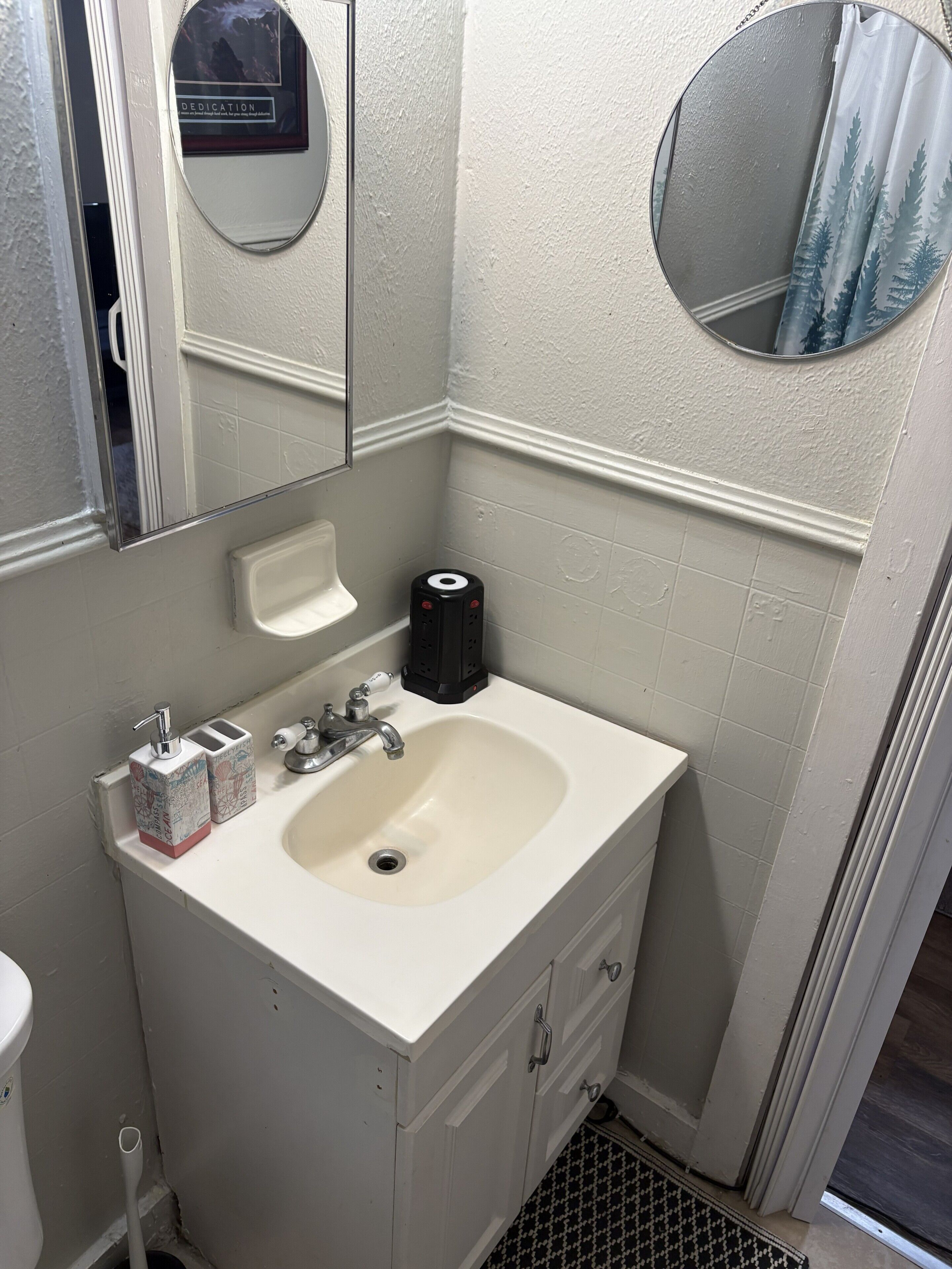 A bathroom with a white sink, a mirror, a toilet, and a small trash bin.