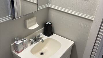 A bathroom with a white sink, a mirror, a toilet, and a small trash bin.