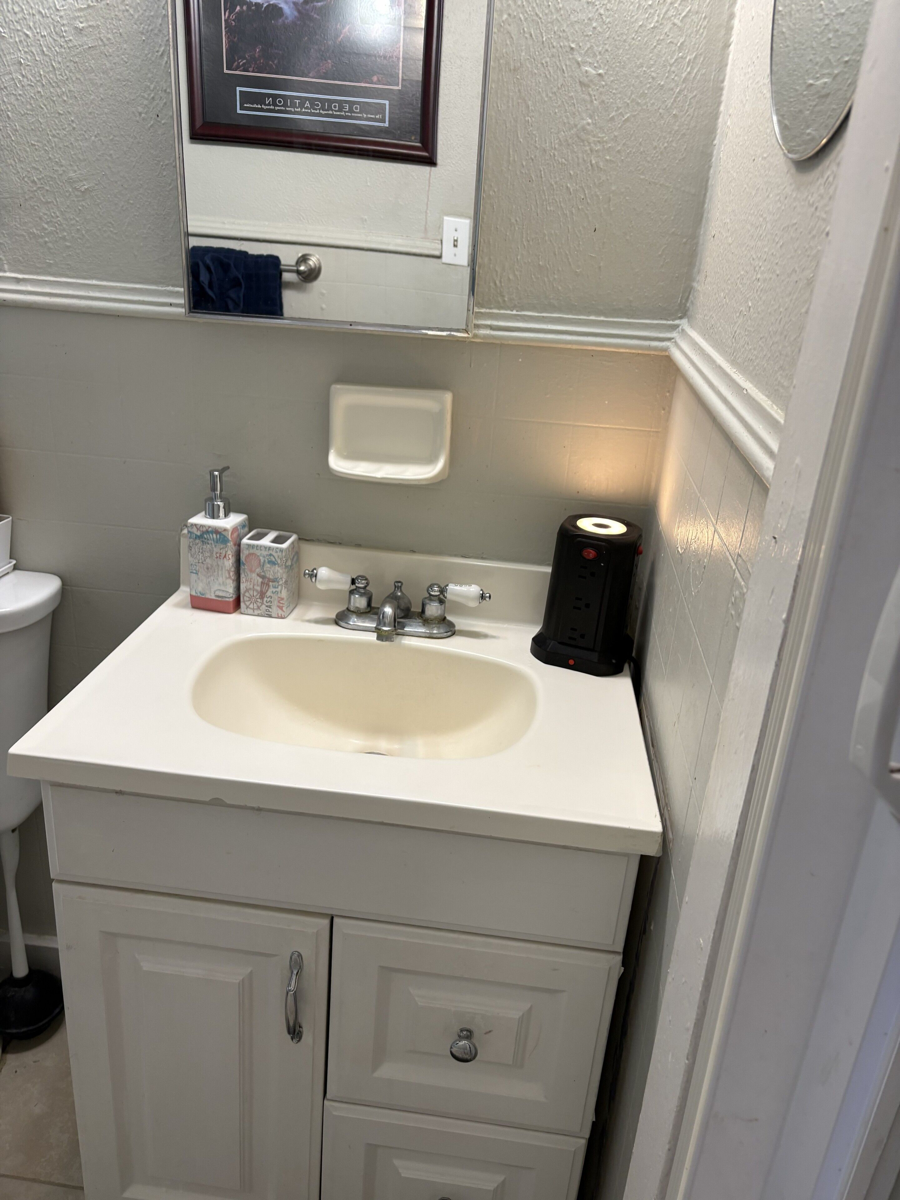 A bathroom with a white sink, a mirror above it, a toilet, and a cabinet below.