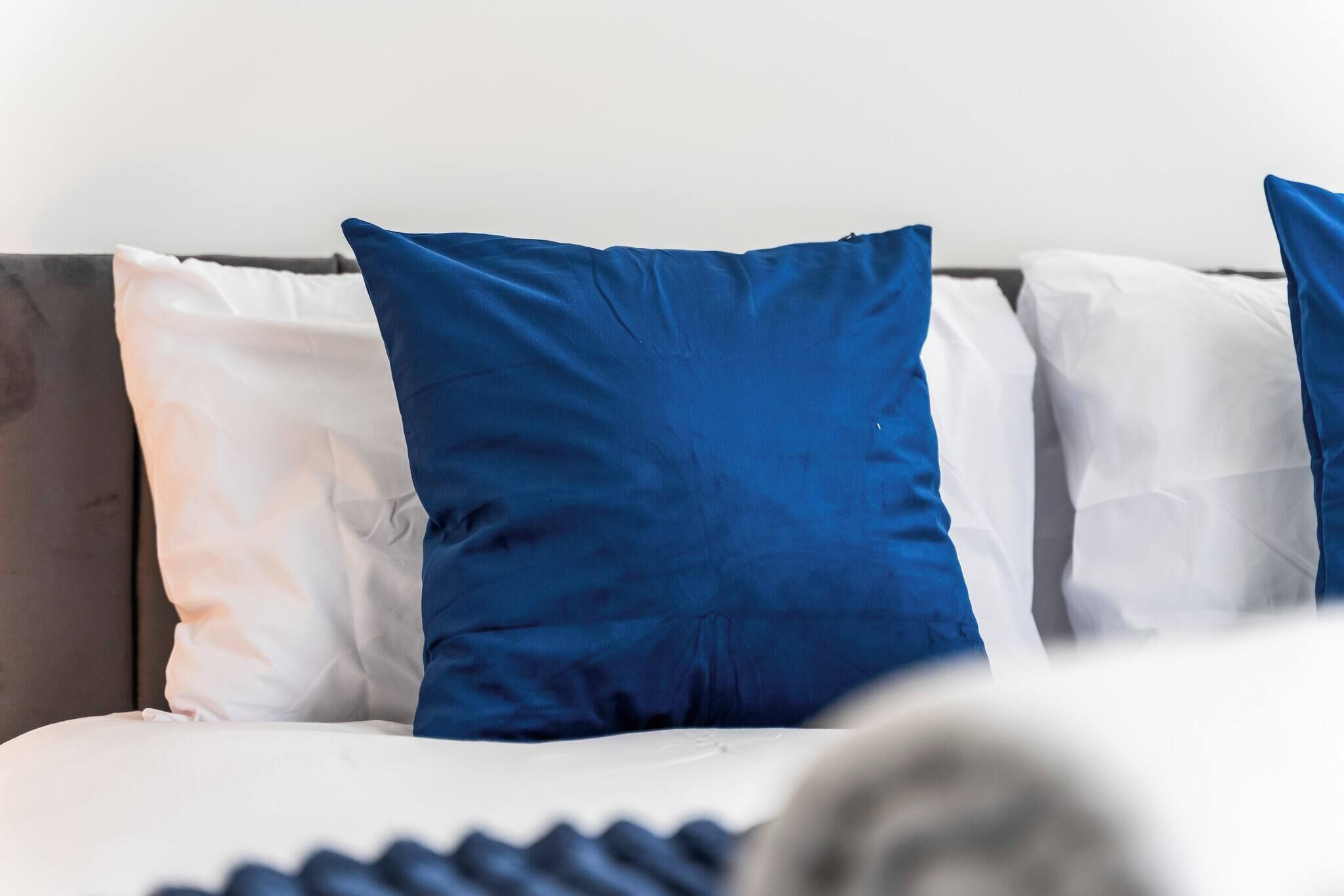 A bed with white and blue pillows, a grey headboard, and a white mattress.