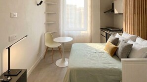Ett kompakt hotellrum med en säng, ett litet bord, en stol, ett skrivbord och ett fönster med gardiner.