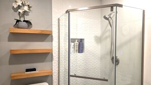 Une salle de bain moderne avec une douche à parois de verre, des toilettes et des étagères en bois où sont rangés les produits de toilette.