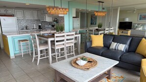 A modern kitchen with white cabinets, a dining area with white chairs, a black leather sofa, and a marble coffee table. - New Listing! Beachfront 2 Bdrm Condo, Family Friendly. Make great memories here! (South Padre Island)