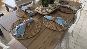 A dining table set with woven placemats, a central plant, and a decorative shell arrangement. - New Listing! Beachfront 2 Bdrm Condo, Family Friendly. Make great memories here! (South Padre Island)