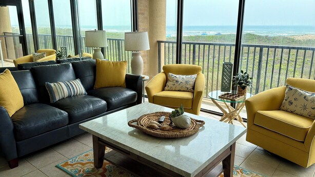 A living room with a black leather sofa, a yellow armchair, and a coffee table with a woven placemat. - New Listing! Beachfront 2 Bdrm Condo, Family Friendly. Make great memories here! (South Padre Island)