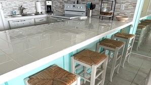A modern kitchen with a white countertop, stainless steel appliances, and a bar area with white stools. - New Listing! Beachfront 2 Bdrm Condo, Family Friendly. Make great memories here! (South Padre Island)