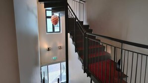 Eine Treppe mit roten Teppichstufen, schwarzen Geländern und einer hängenden Leuchte.