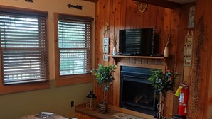 A cozy living room with a fireplace, wooden walls, a television, and a red chair. - 1BR Cabin W/ Loft For 2 Great Views Over Resort (Davis)