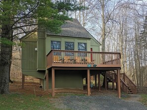 A cabin with a deck, a staircase, and a view of the surrounding forest.