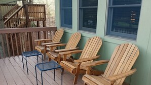 A wooden deck with Adirondack chairs and a blue chair, a wooden staircase, and a window with blinds. - 1BR Cabin W/ Loft For 2 Great Views Over Resort (Davis)
