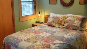 A bedroom with a floral quilt, a wooden headboard, a nightstand with a lamp, a window with blinds, and a wreath on the wall. - 1BR Cabin W/ Loft For 2 Great Views Over Resort (Davis)