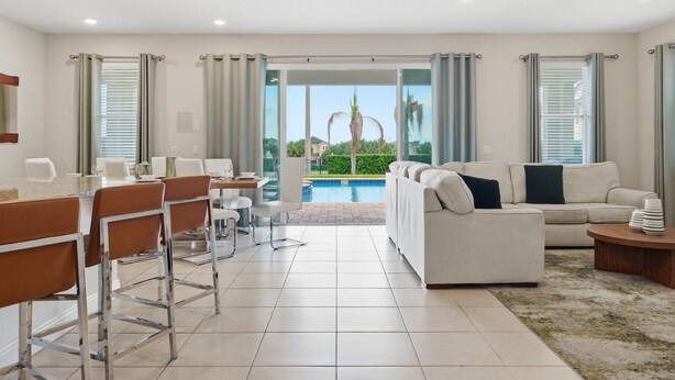 En moderne stue med sofa, spiseområde og udsigt til en swimmingpool.