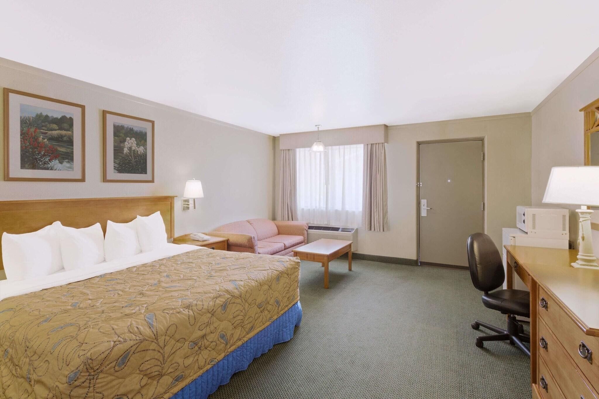 Habitación de hotel con cama, escritorio, sillón, sofá y dos cuadros en la pared.