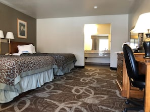 A hotel room with two beds, a desk with a chair, a bathroom with a sink and mirror, and a patterned carpet. - Days Inn Provo (Provo)