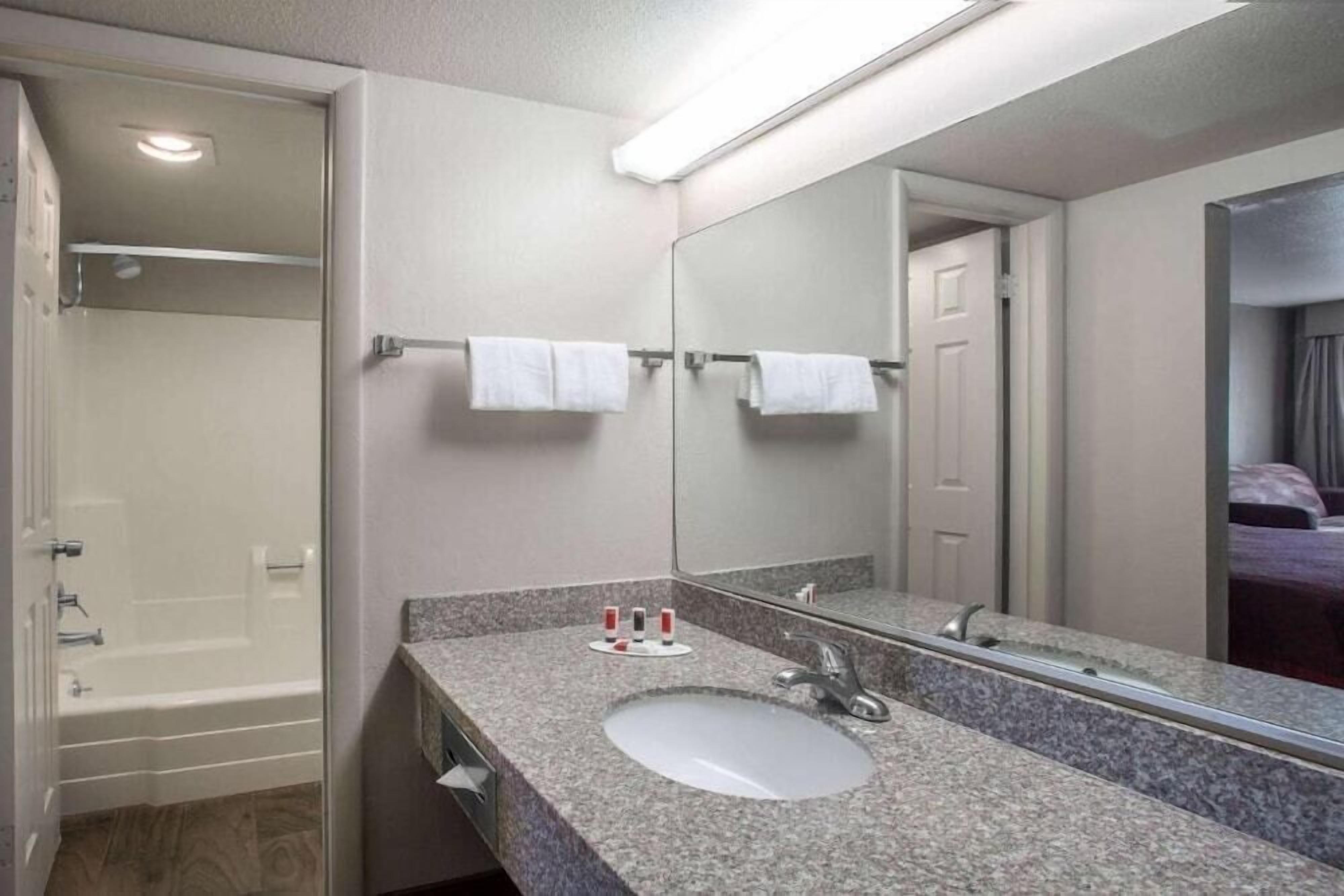Een badkamer met een wastafel met granieten blad, een spiegel en een douche die door een open deur zichtbaar is.