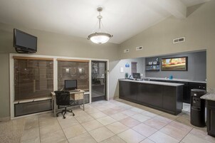 A hotel room with a desk, computer, and a large window with blinds.