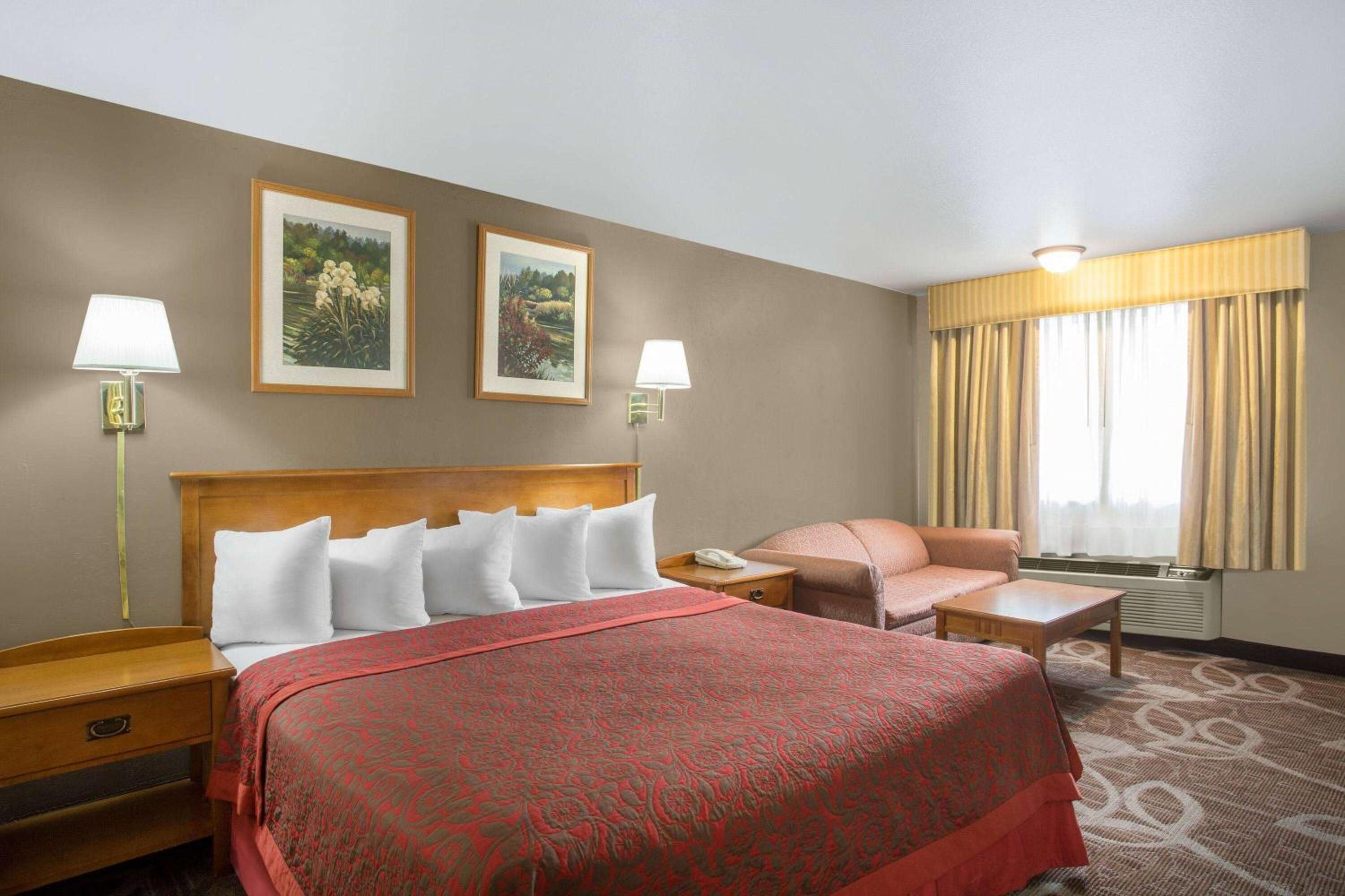 Ein Hotelzimmer mit einem Bett, zwei Nachttischlampen, einem Nachttisch, einem Schreibtisch, einem Stuhl und zwei gerahmten Bildern an der Wand.