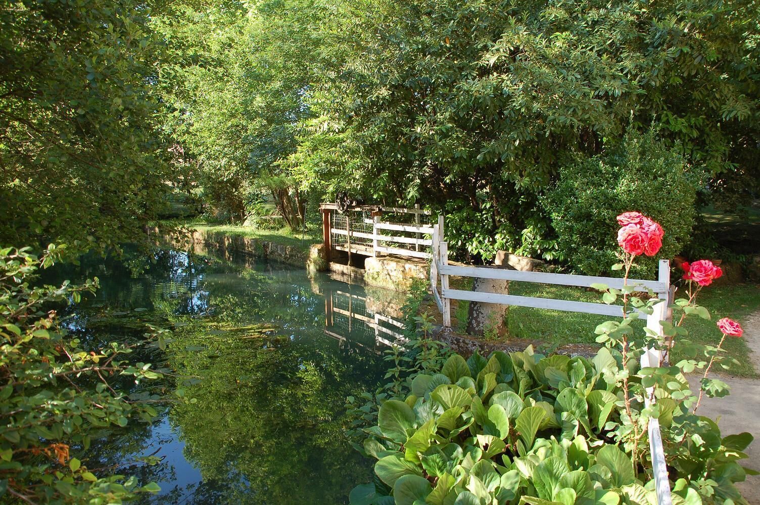 A serene waterway with a wooden bridge and lush greenery.