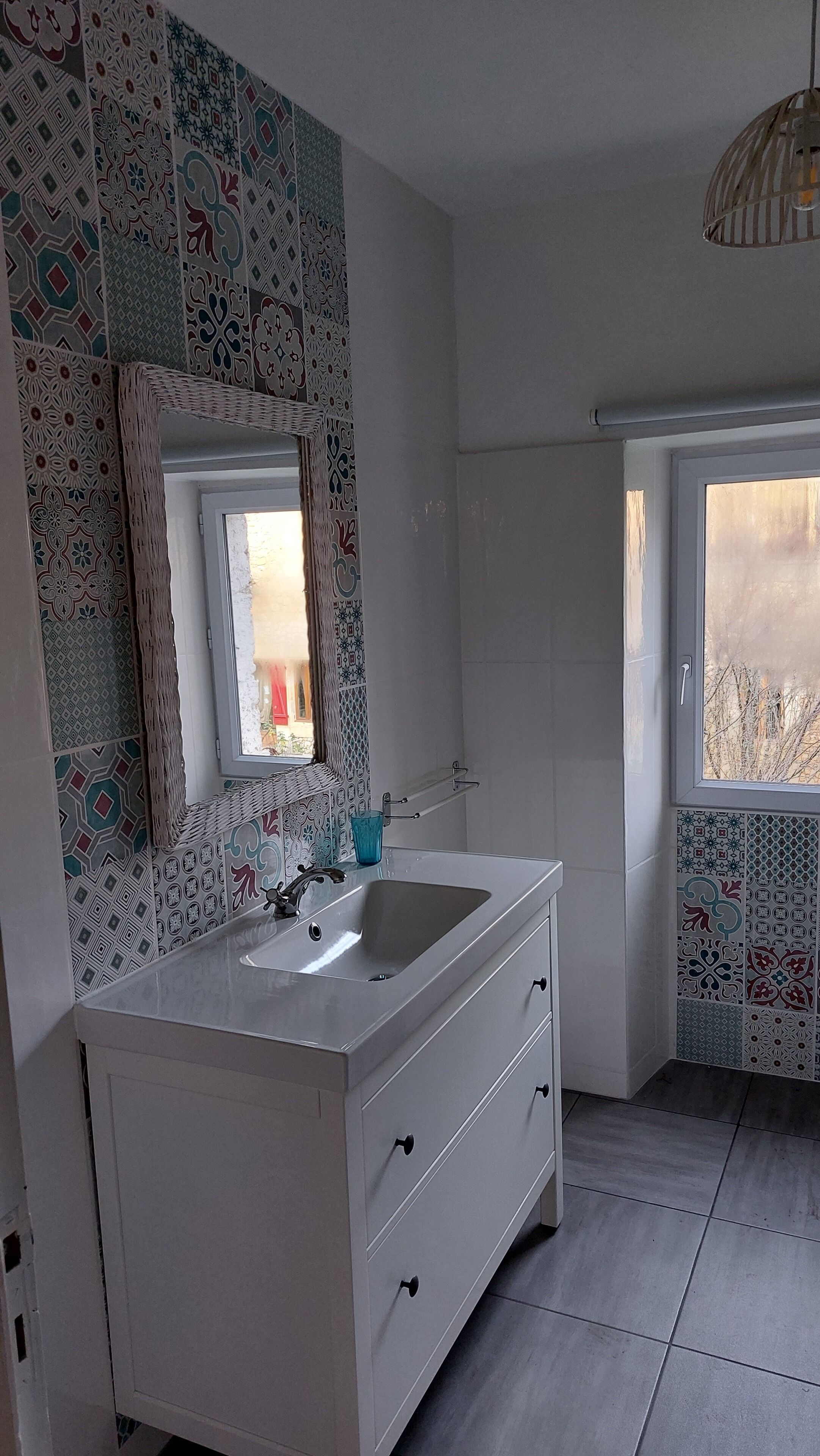 A bathroom with a white vanity, a mirror, and patterned tiles on the walls.