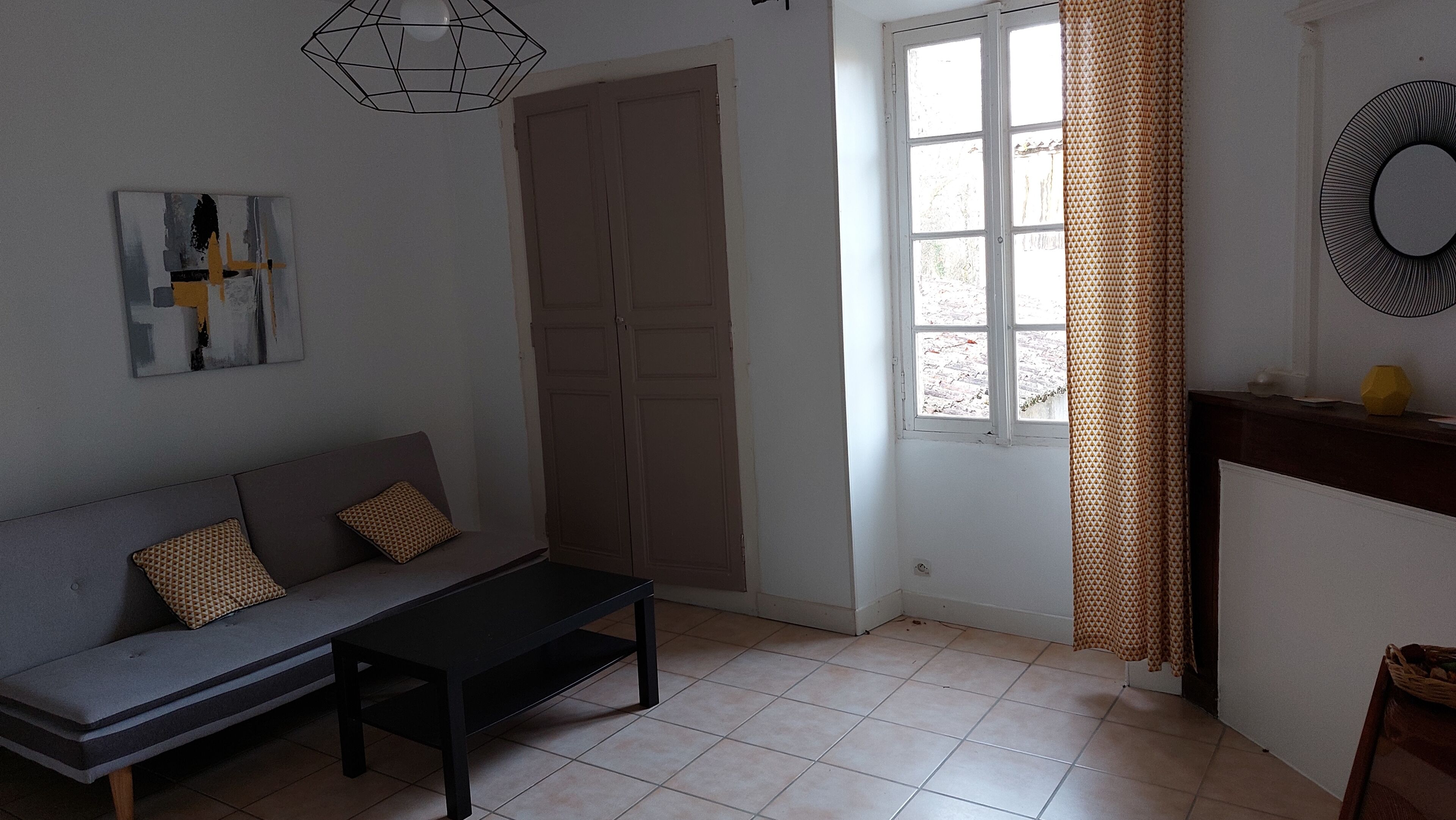 Una habitación con un sofá, una mesa de centro, una puerta, una ventana con cortinas y un espejo montado en la pared.