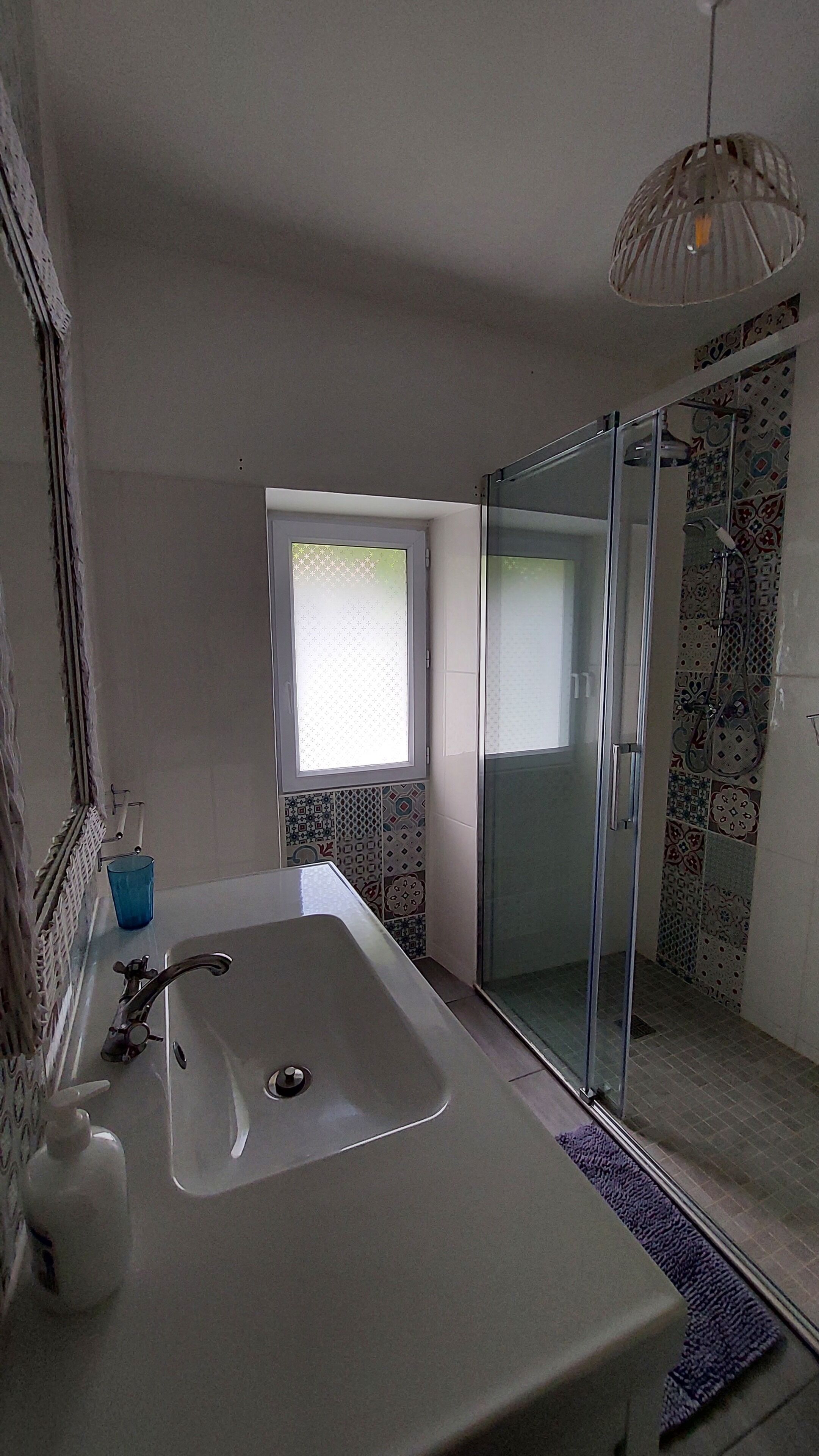 A bathroom with a large sink, a shower, and a window.