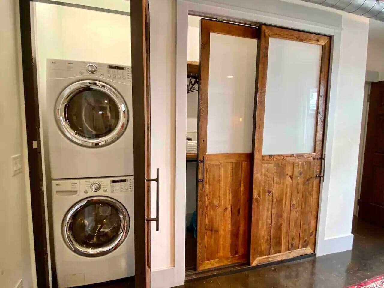 A laundry room with two stacked front-loading washing machines and a wooden sliding door.
