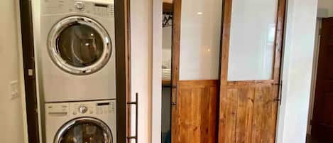 A laundry room with two stacked front-loading washing machines and a wooden sliding door.