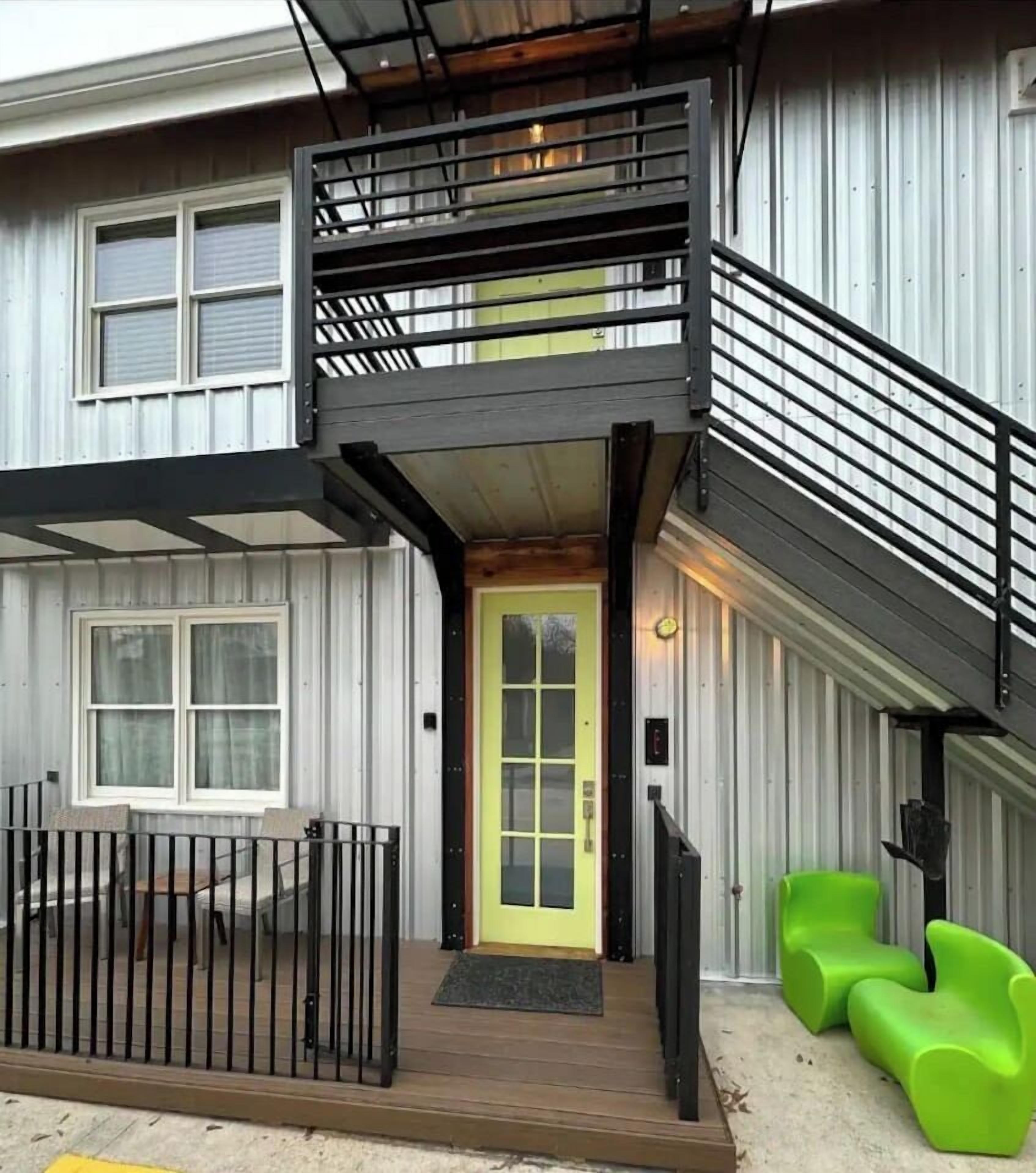 A two-story building with a balcony, a yellow door, and green seating.