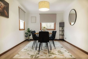 Un espace repas comprenant une table, des chaises, un tapis, un luminaire suspendu, une fenêtre et un miroir au mur.