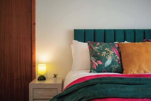 Un lit bien fait, avec une tête de lit verte, une lampe de chevet et un coussin à motifs floraux.