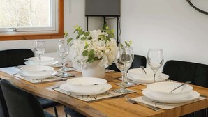Une table à manger dressée avec de l’assiette blanche, des verres et des couverts, un vase rempli de fleurs blanches et un téléviseur fixé au mur.