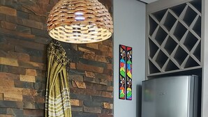 A dining area with a wooden table, chairs, a woven light fixture, a refrigerator, and a brick wall. - Great location, Caxias do Sul (Caxias do Sul)