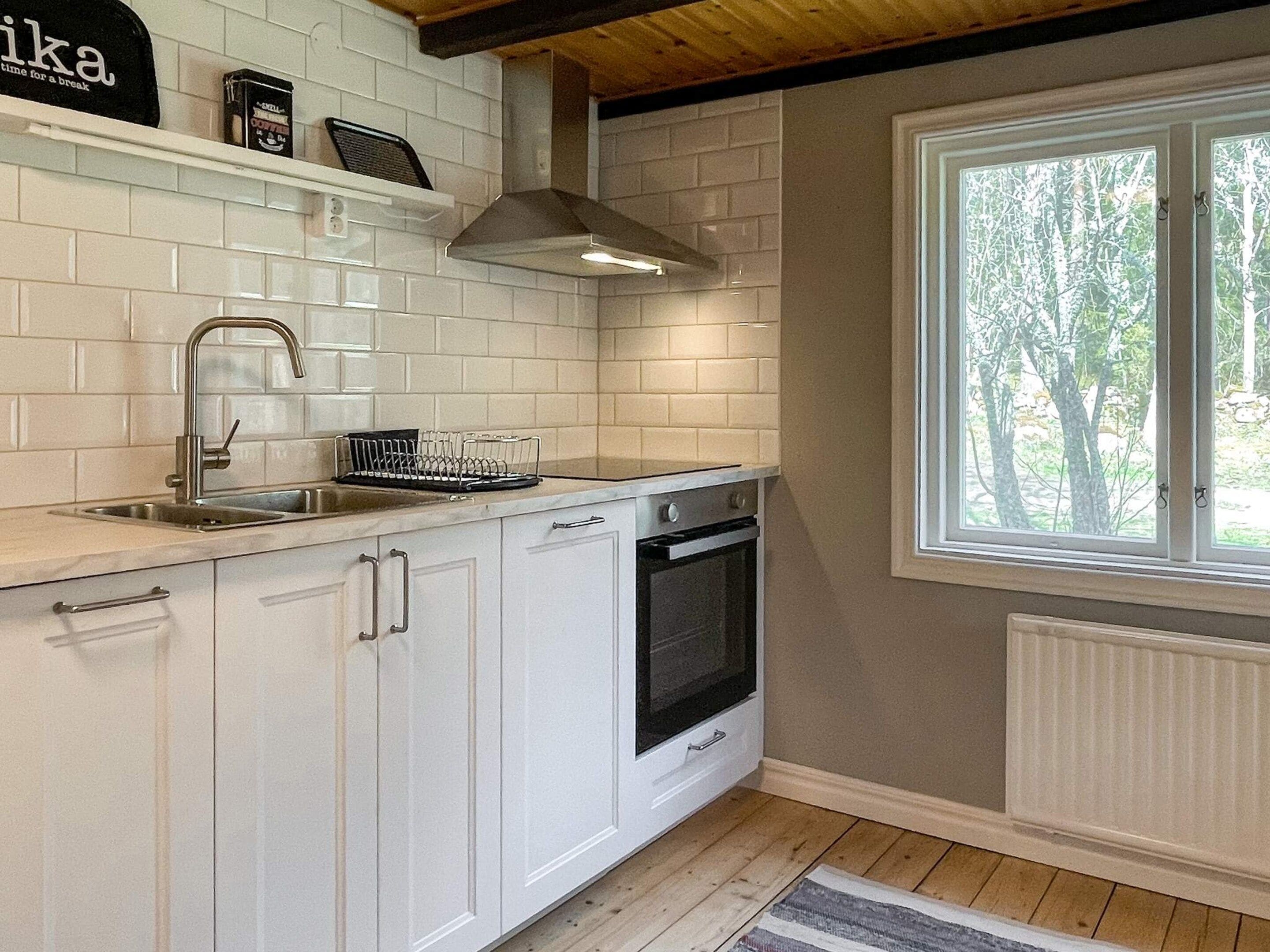 Eine Küche mit weißen Schränken, einer Edelstahl-Spüle, einem eingebauten Backofen und einem Fenster mit Blick auf Bäume.