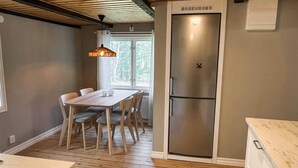 A compact kitchen with a wooden table, chairs, a refrigerator, and a hanging light fixture. - 4 Star Holiday Home in Emmaboda (Emmaboda)