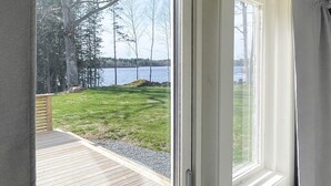 A view through a window of a wooden deck leading to a grassy area with a lake and trees in the background. - 4 Star Holiday Home in Emmaboda (Emmaboda)